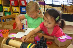 Two girls cutting and drawing at the writing table