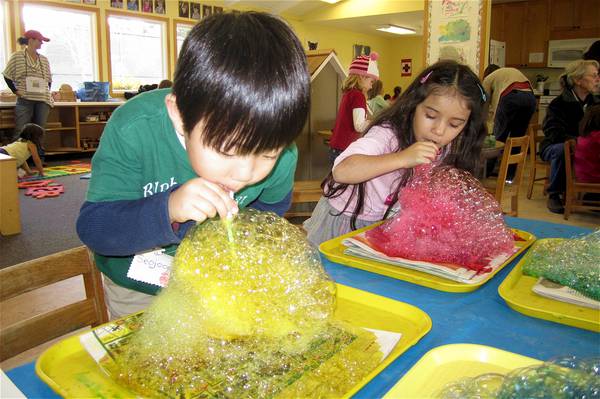 Two children blowing rainbow-colored bubbles with a straw