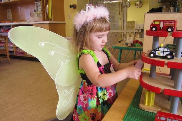 Girl dressed in fairy wings playing with cars