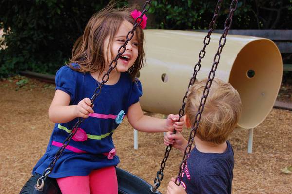 Two children laughing on the tire swing